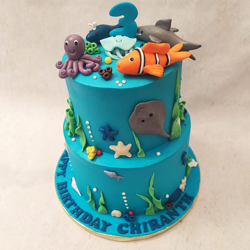 The top tier of this two tier sea theme cake showcases a playful gathering of clown fish, their vibrant colors dancing amidst the coral reefs. 