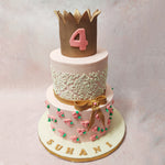 A light pink tier at the bottom of this 3 tier crown cake features bright pink buttercream roses blooming 