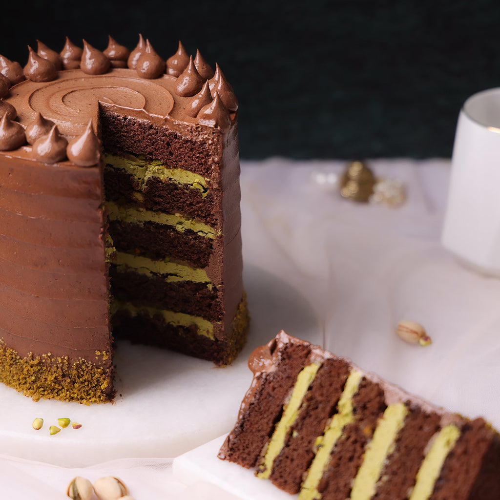 A slice cut from a chocolate pistachio cake, revealing alternating layers of chocolate and pistachio