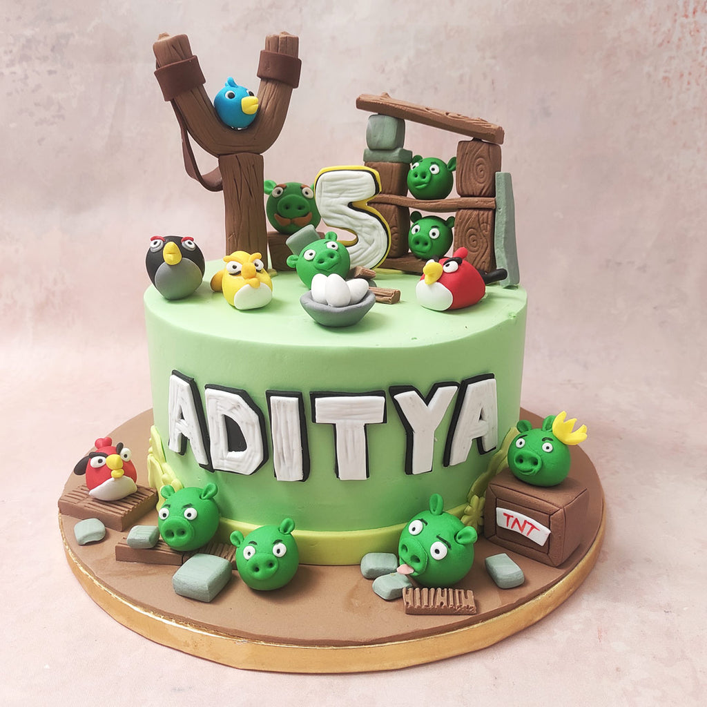 The green base of this Angry Bird Cake sets the stage for an epic showdown, mirroring the iconic wooden barracks, the strategic catapult, and the assortment of colourful characters that define this gaming universe.