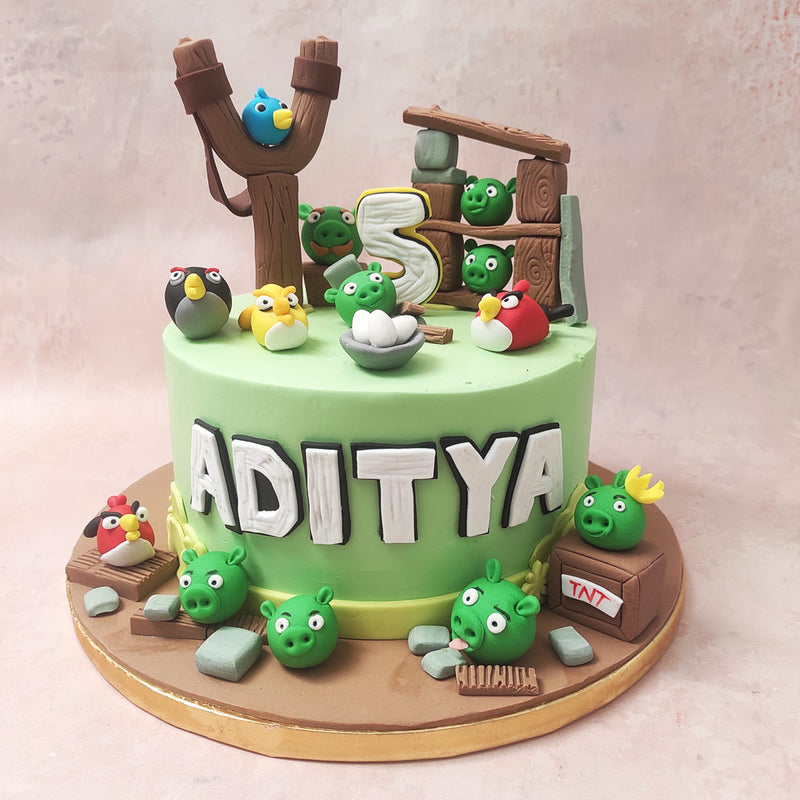 The green base of this Angry Bird Cake sets the stage for an epic showdown, mirroring the iconic wooden barracks, the strategic catapult, and the assortment of colourful characters that define this gaming universe.
