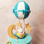 Picture-perfect tiers, reminiscent of a serene blue sky dotted with fluffy clouds, set the stage for a magical journey through the heavens via this Blue Hot Air Balloon Cake.