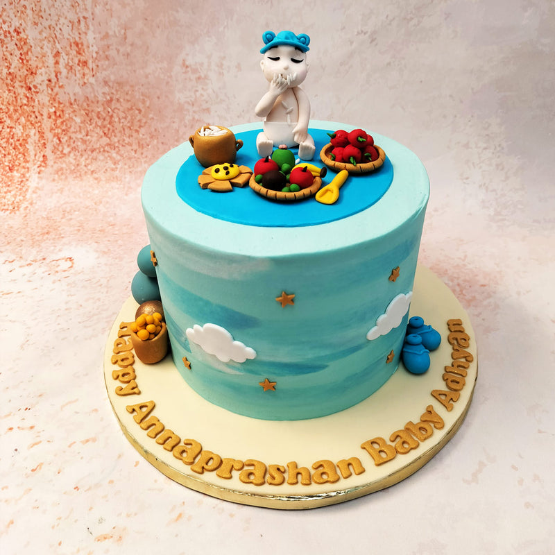 The baby atop this Annaprasanna Cake with his innocent charm, is surrounded by traditional food items such as rice, fruits, and a small clay pot, each meticulously detailed to reflect the importance of the ceremony.