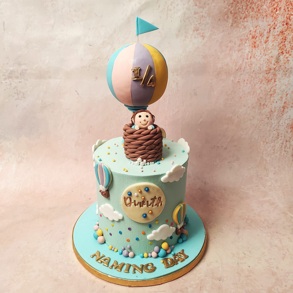 The tall, light sky blue base of this Hot Air Balloon Theme Cake, adorned with fluffy white clouds, sets the stage for an enchanting aviation adventure. 