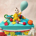 The playful inclusion of everyday objects like rattles, colourful balls, and a tiny truck in the design of this Baby Clothes Cake speaks to the heart of a child’s imagination, turning simple items into moments of joy. 