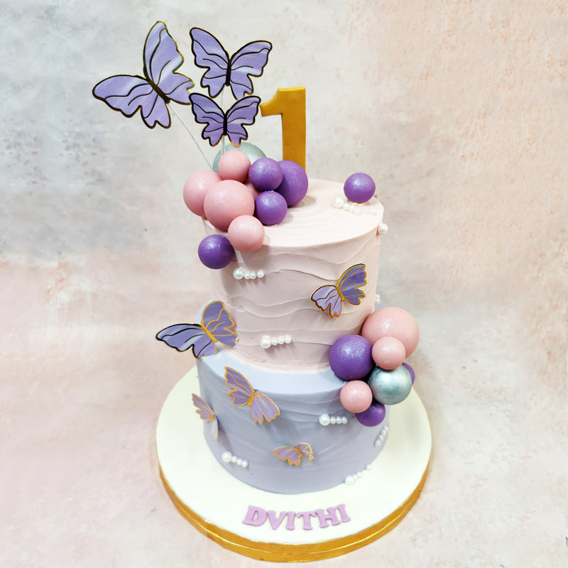 Birthday cake with pink and purple decorations, including butterflies and balloons, on a light background.