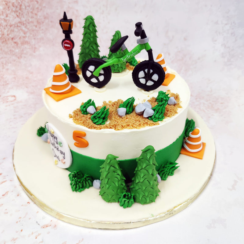 For the nature-lover, this design would make an excellent Birthday Cake For Him / Birthday Cake For Her. The edible bike rests upon a sandy trail, sprinkled with tiny grey pebbles and patches of lush greenery, creating the illusion of a forest pathway. 