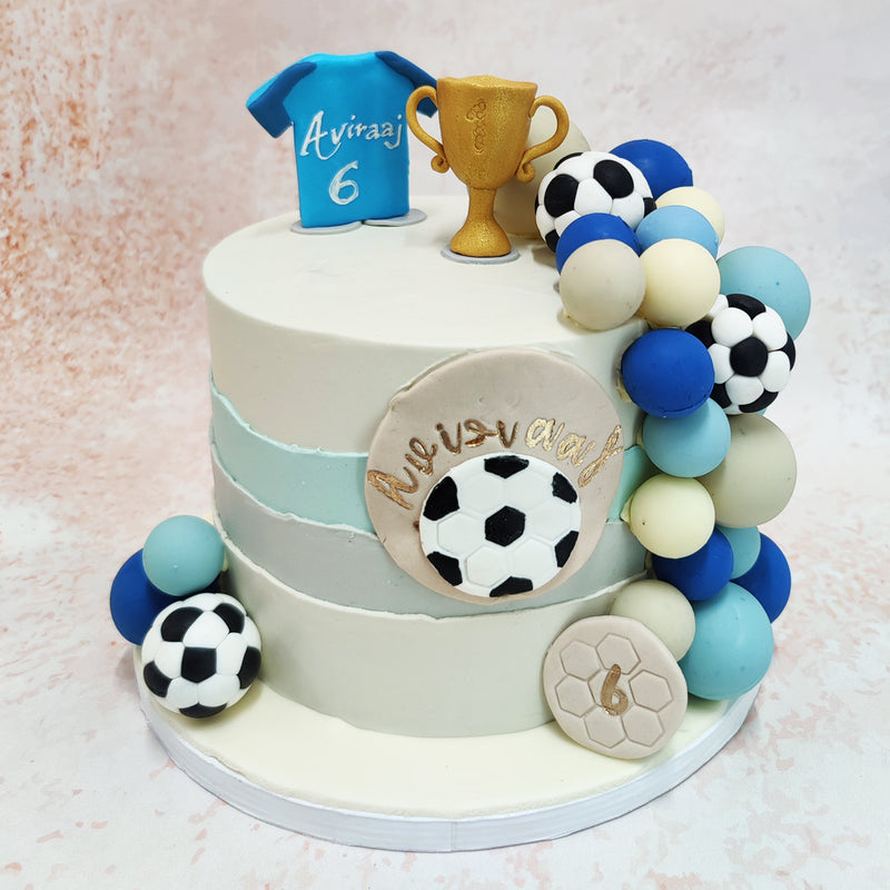 The cascading cluster of footballs, in a harmonious blend of black, white, and blue, adds a dynamic element to this Birthday Cake For Him, echoing the excitement and energy of the game.
