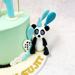 The second companion panda of this Birthday Cake For Kids sits playfully to the side holding turquoise utensils, embodying the spirit of celebration and companionship.