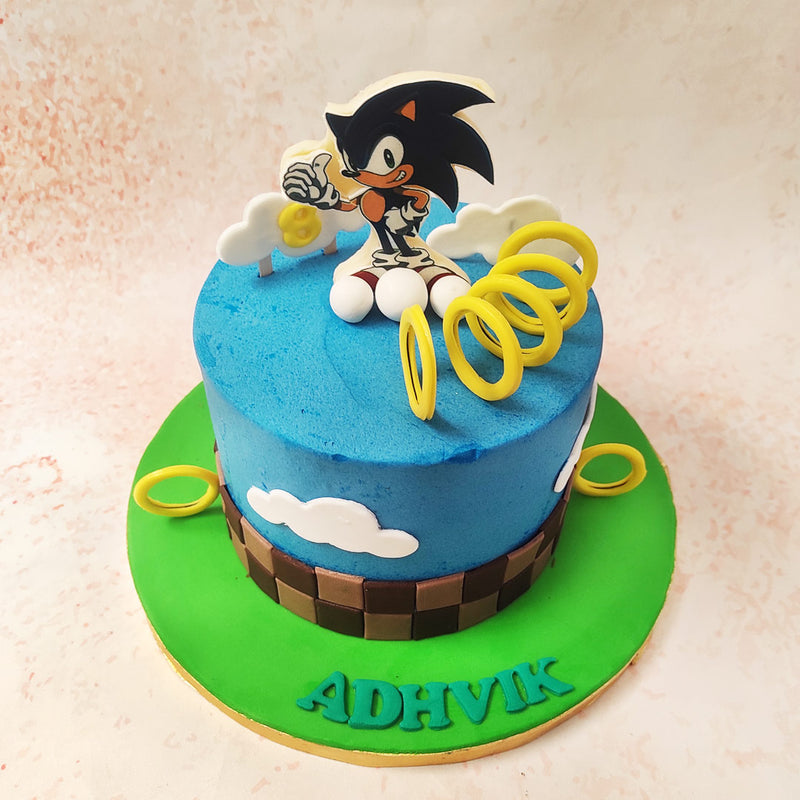 The top tier of this Sonic Birthday Cake For Kids is expertly decorated to resemble a bright blue sky dotted with fluffy white clouds, adding a whimsical touch that instantly transports you to the bustling realms of Green Hill Zone.