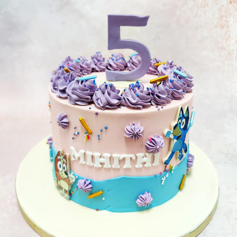 This two-tiered Birthday Cake For Kids harmoniously blends soft pastel hues, with a dreamy pink base adorned with expertly piped lavender rosettes crowning the top tier. 