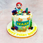 The sides of this Birthday Cake For Kids transform into an aquatic playground, complete with coral, seaweed, bubbles, and those unmistakable cartoon fish eyes peeking out from the ocean floor. Textures of sand-like crumbs and rounded fondant shells add depth to the underwater world, while the soft ombré of ocean blue blends seamlessly into creamy white frosting above. 