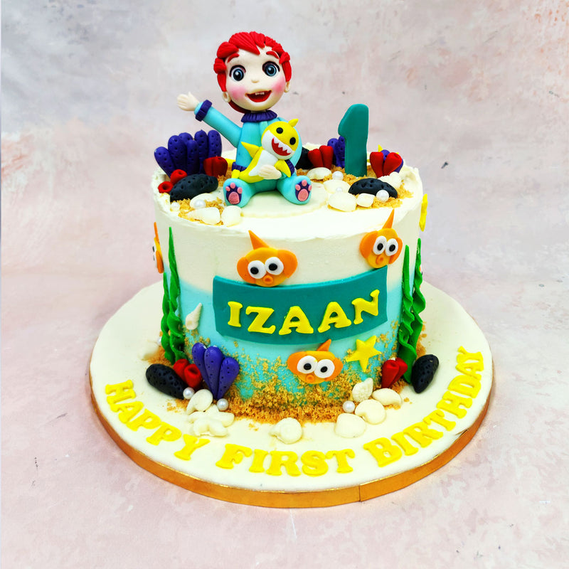 The sides of this Birthday Cake For Kids transform into an aquatic playground, complete with coral, seaweed, bubbles, and those unmistakable cartoon fish eyes peeking out from the ocean floor. Textures of sand-like crumbs and rounded fondant shells add depth to the underwater world, while the soft ombré of ocean blue blends seamlessly into creamy white frosting above. 