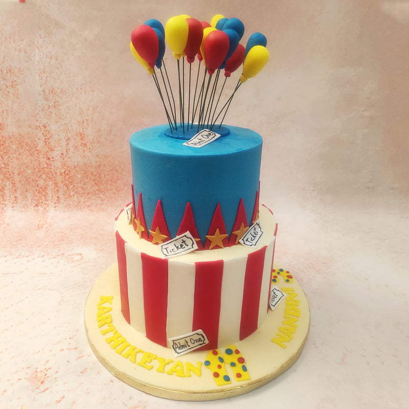 Atop this Big Top Circus Cake, a vibrant cluster of balloons in red, blue, and yellow adds a joyful touch, symbolising the carefree spirit and fun of childhood. 