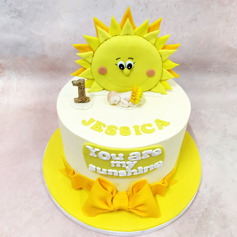 Set against a pristine white background, this Birthday Cake For Kids showcases meticulous attention to detail with a delicate sleeping baby figurine, symbolising the peaceful slumber of infancy beneath the watchful gaze of the sunshine. 