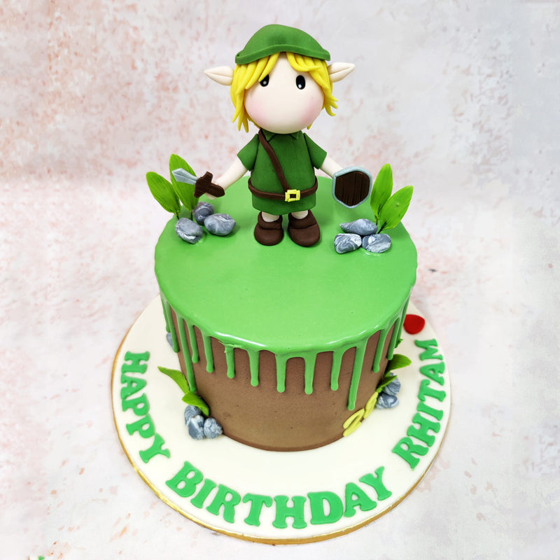 This Birthday Cake For Kids features a striking two-tone design with a rustic brown base resembling the earthen terrains of Hyrule, topped with vibrant green drip icing reminiscent of the Great Deku Tree’s foliage. 
