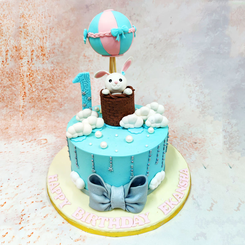 The design of this Birthday Cake For Kids showcases a dreamy sky-blue canvas decorated with cascading fluffy white clouds and a silver elements that create the illusion of gentle rain or twinkling stars.