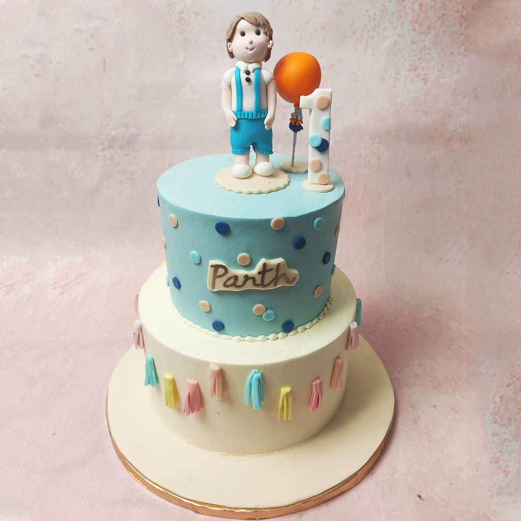 The top tier of this Boy and Balloon Cake is dressed in a dark blue hue with white and light blue polka dots embellishing it.