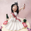The bride to be figurine of this bride to be cake is holding up a glass of wine, seemingly poured from the empty bottles strewn around her amidst the building black with the bride and groom's initials on them.