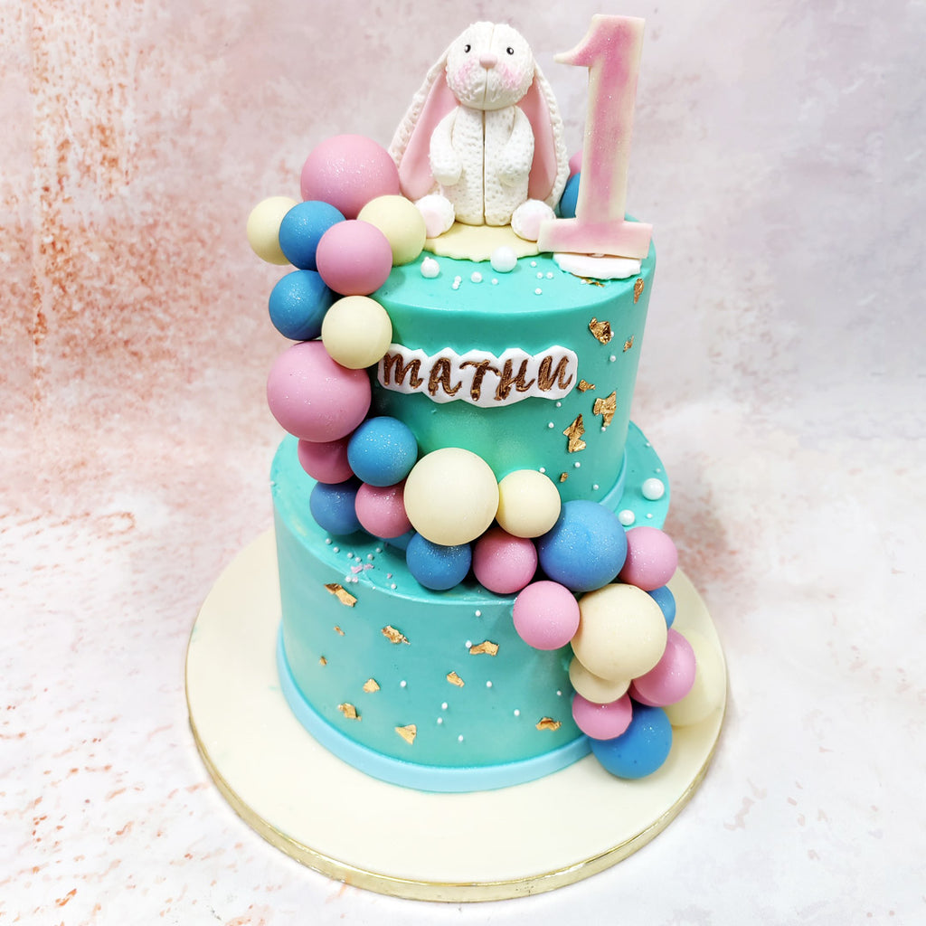 Draped in serene turquoise, each tier of this Bunny Birthday Cake showcases a cascading array of perfectly crafted balloon spheres in pastel pink, cream, and powder blue. 