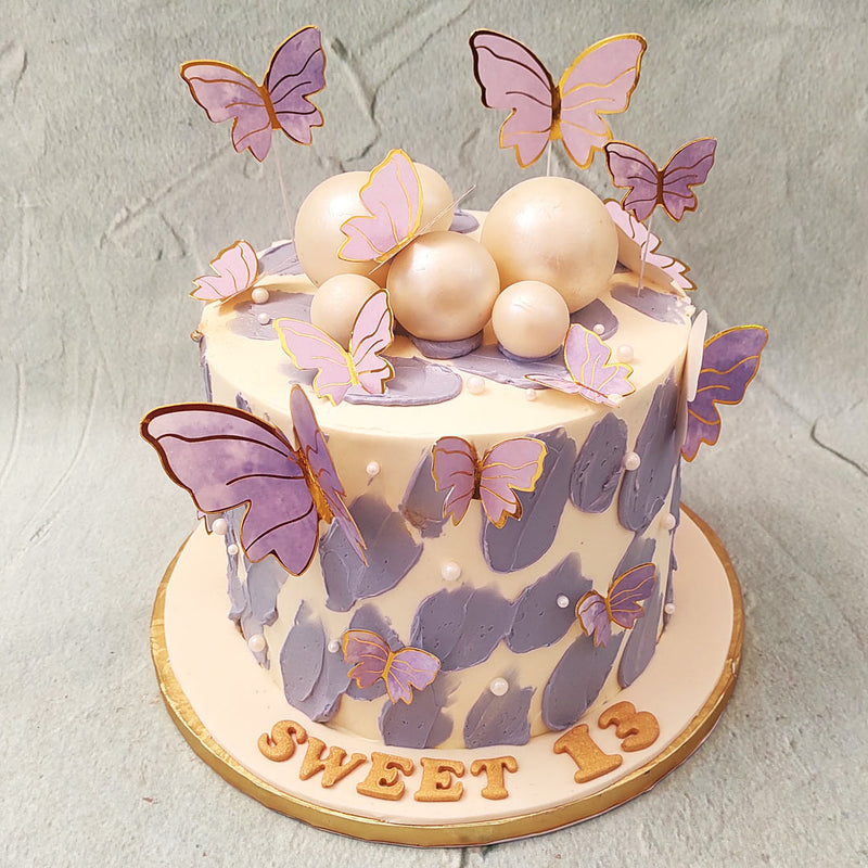 To further enhance its allure, this purple butterfly birthday cake is embellished with large edible pearls that glisten like hidden treasures amidst the buttercream smudges. 