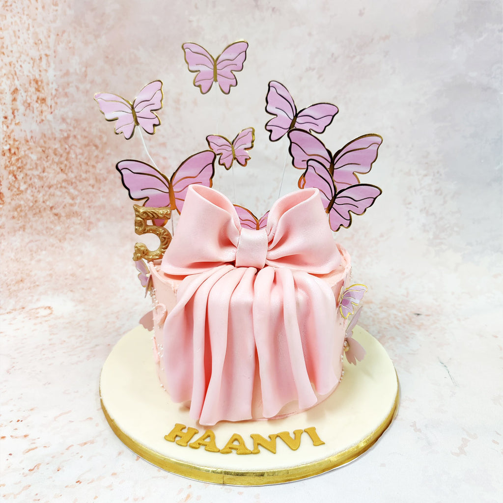 Draped in soft blush pink fondant, this Butterfly Bow Cake exudes sophistication, with a large, delicately pleated bow at its centre. 