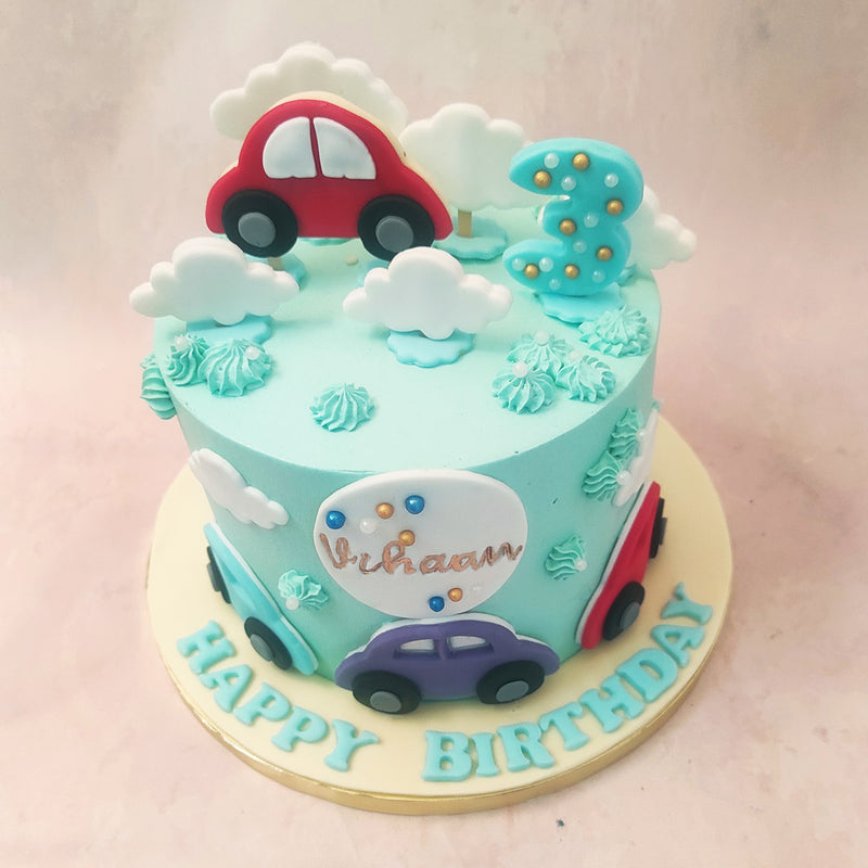 A car theme birthday cake for kids, this design features a sky blue base ornamented with fluffy, white clouds and buttercream swirls.