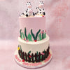 Both tiers of this two tier cow theme cake are set on a farm, with the bottom tier frosted in white buttercream and the top tier in pink. 