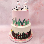 Both tiers of this two tier cow theme cake are set on a farm, with the bottom tier frosted in white buttercream and the top tier in pink. 