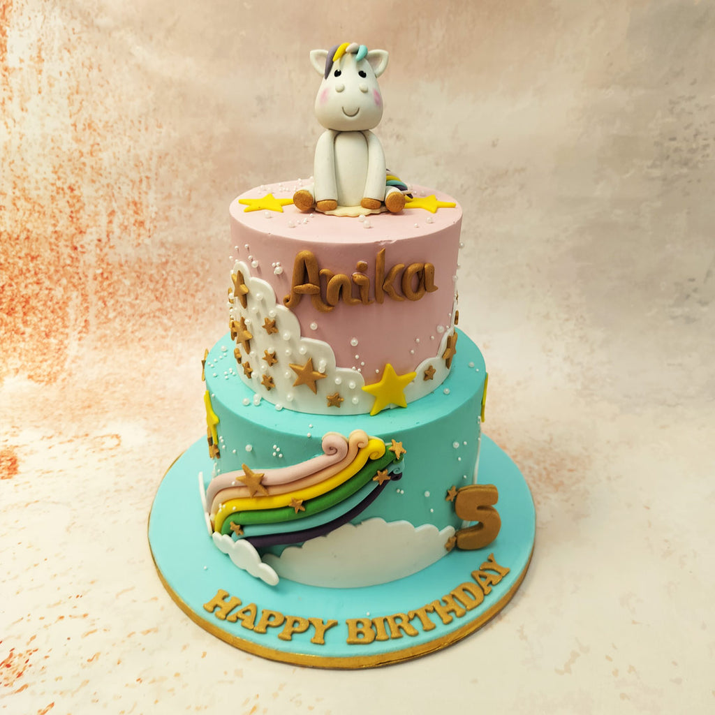 The blue bottom tier of this Unicorn Rainbow Cake features a colourful rainbow shooting out of it and the top pink tier is bursting forth with gold stars.