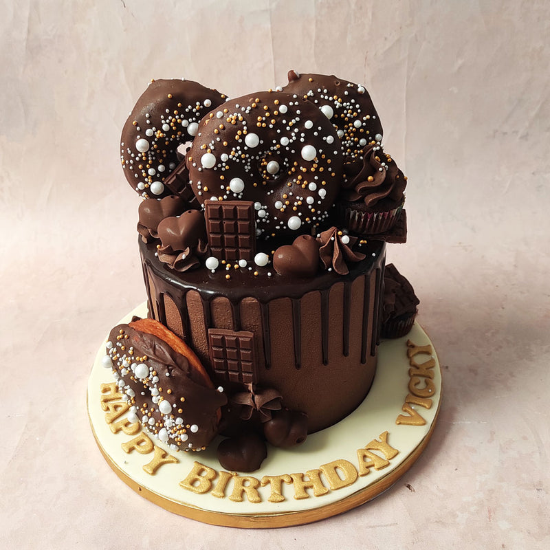 Our Chocolate Drip Cake features real chocolate glazed donuts, adorned with opulent gold, silver, and white pearl sprinkles, strategically placed to create a gustatory galaxy. 