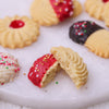 Close-up of a broken Christmas shortbread cookie showing the rich, buttery texture and red icing with gold sprinkles.