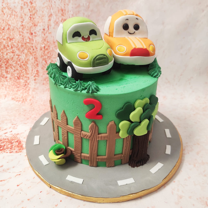 The top of this Cute Car Cake is adorned with two cute, smiling cars, one in vibrant orange and the other in a cheerful lime green, both designed in classic Kawaii style with oversized, expressive eyes that give them a joyful, animated feel. 
