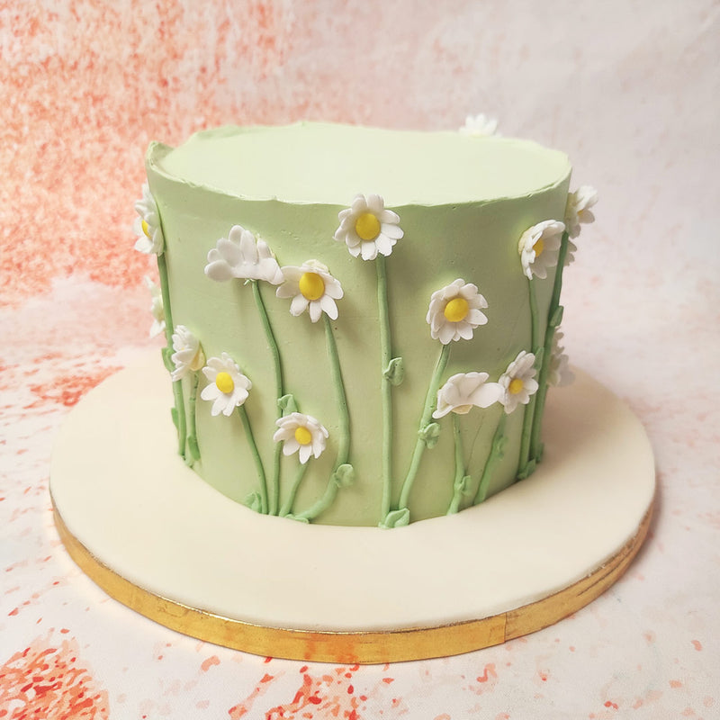 This enchanting Daisy Theme Cake features a soft green base that serves as a serene backdrop for an array of white daisies, each one meticulously crafted and placed with care. 