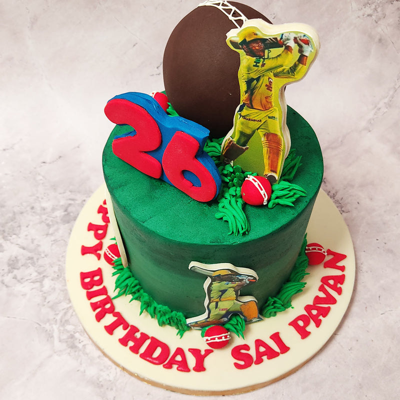 Adding to its charm, a large brown cricket ball is perched atop this cricket theme cake, while contrastingly nestled in some buttercream grass on this Dhoni theme cake is a small red cricket ball.