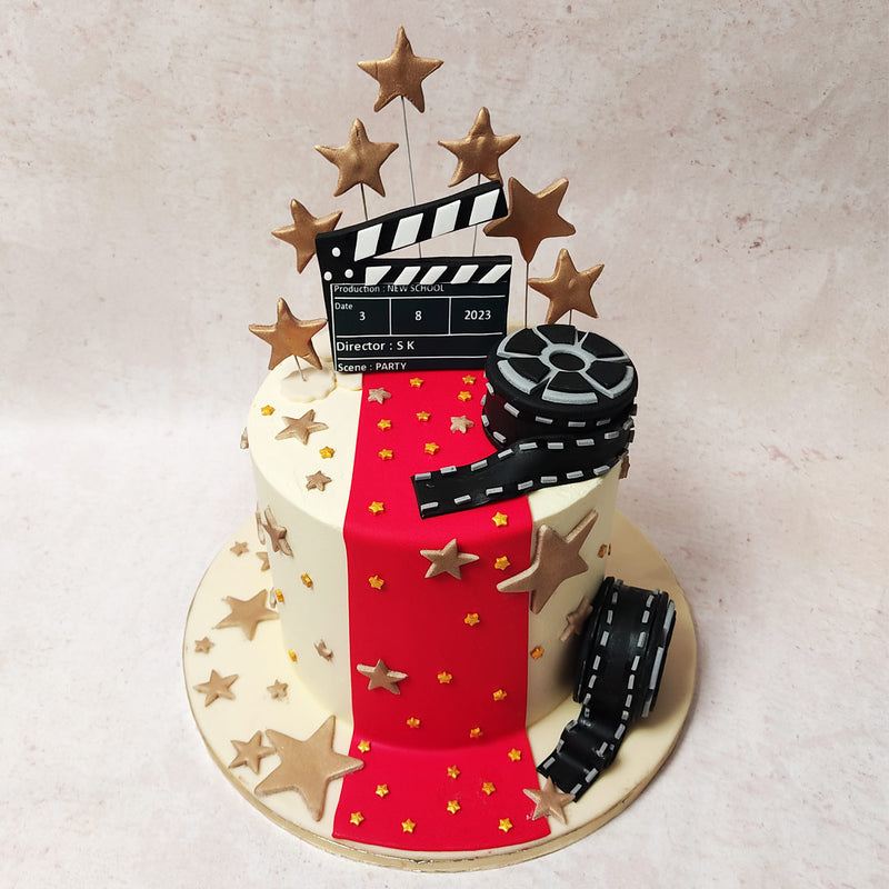 The foundation of this movie theme cake design is a pristine white canvas with a mesmerising red carpet that cascades down its sides. 