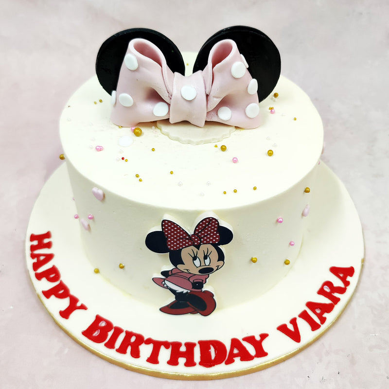 The highlight of this Disney Minnie Cake is the oversized pink fondant bow with white polka dots, nestled between glossy black Minnie ears—an iconic silhouette that needs no introduction. Lightly scattered around the soft vanilla base are golden and blush sugar pearls, adding just the right amount of sparkle.