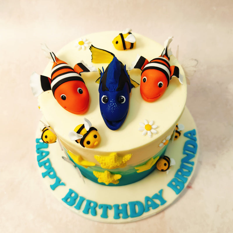 At the heart of this enchanting Dory Cake swims a majestic blue tang fish, flanked by two playful clownfish, reminiscent of beloved characters from a famous tale. 