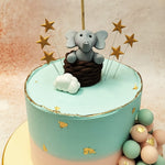 The pale blue and pink tiers are delicately adorned with gold leaf accents, adding a touch of elegance to the playful design of this Elephant Hot Air Balloon Cake.