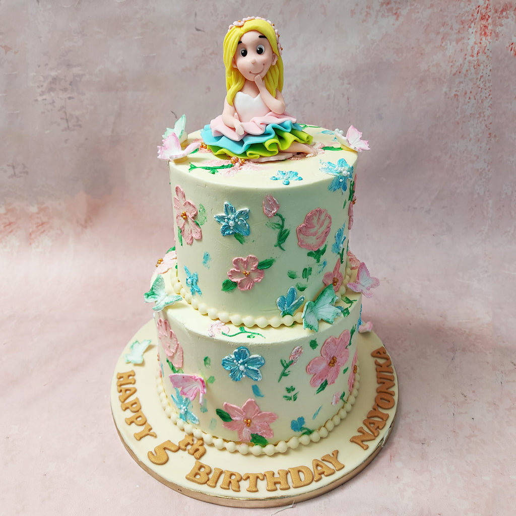 Hand-drawn buttercream flowers in soft pink and blue hues cascade gracefully down the tiers, creating a whimsical garden scene on this Fairy Cake. 