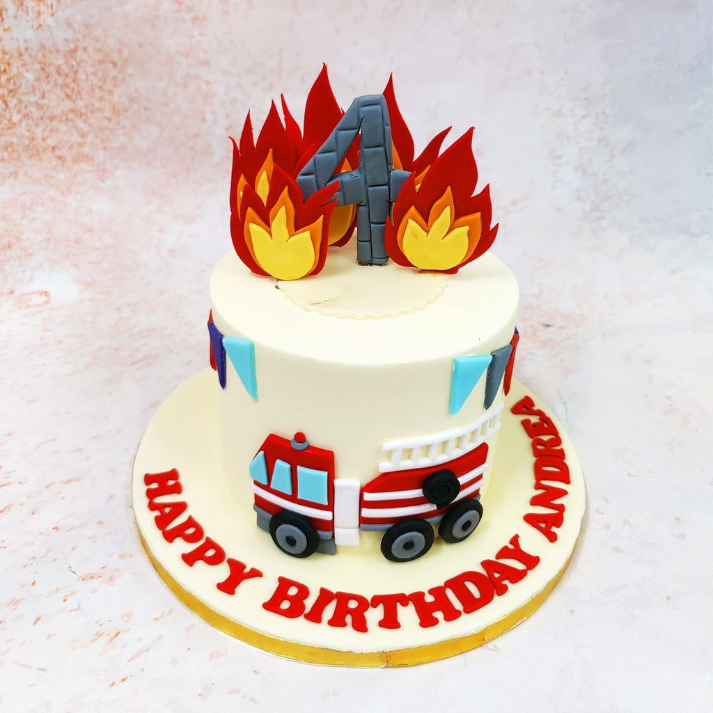 The centrepiece of this Firetruck Cake features dramatic flames crafted in vibrant reds and yellows, creating a striking visual impact against the clean ivory backdrop.