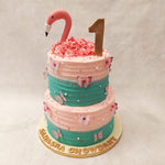This two tier Flamingo Cake features a unique color palette, with a vibrant green at the bottom tier representing the lush environment where flamingos thrive, while the pink top tier symbolizes their elegant and graceful appearance. 
