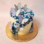 This enchanting creation features a light, neutral yellow base that’s adorned with a delicate grey and blue buttercream rosette, this butterfly swirl cake is a visual delight that will captivate your senses.