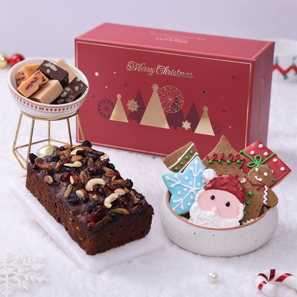 Luxury Gourmet Christmas Gift Hamper featuring a plum cake, assorted fudge in a bowl, and decorated sugar cookies in front of a red gift box.