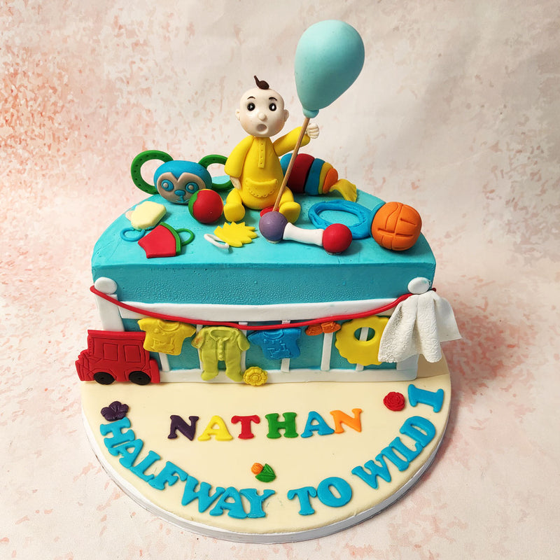 The top of this Half Year Birthday Cake is scattered with colourful toys, from a cheerful green monkey to a basketball, creating an interactive scene that feels alive with the energy of a toddler’s world. 