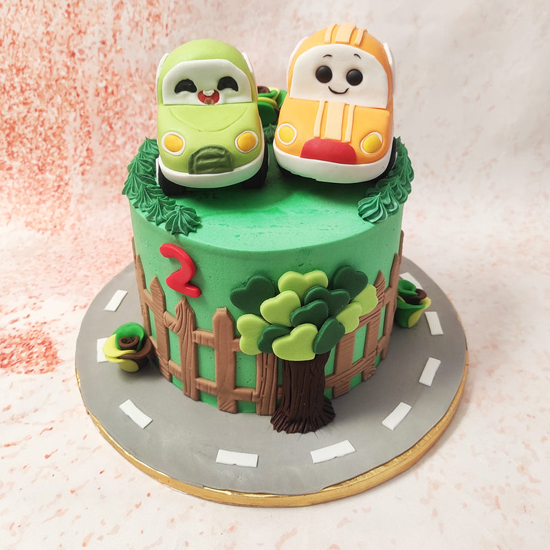 The base of this Kawaii Cake features a whimsical outdoor scene with a charming wooden fence, leafy green trees, and a smooth grey road that winds around the base, symbolising adventure and a sense of carefree fun.
