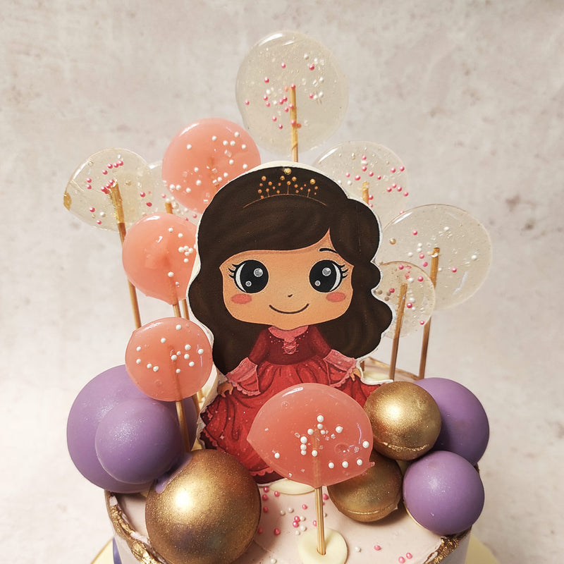 This majestic lollipop cake is embellished with opulent gold and royal purple baubles, symbolising the grandeur of a princess's world. 