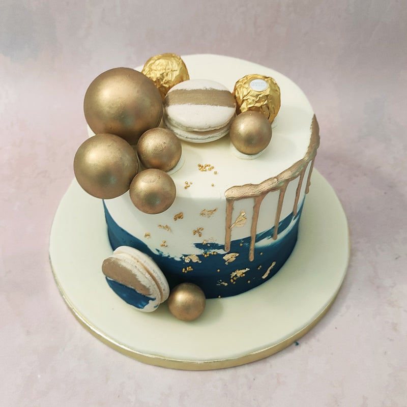 The elegant and artistic aesthetic of this blue and gold drip cake is further complemented by the ornamentation of the gold leaves and baubles.