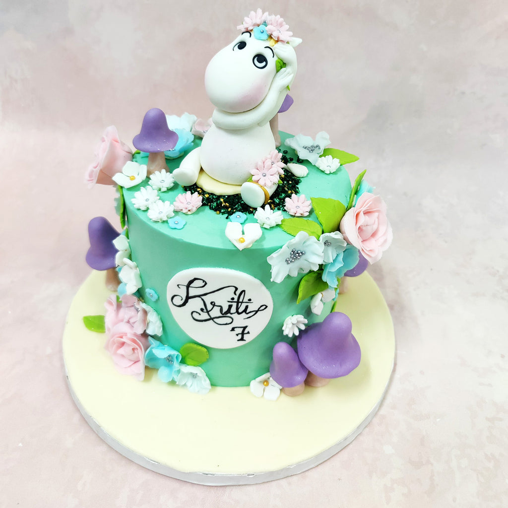 The star of this Moomins Cake is an adorable Moomin character, complete with a dainty flower crown, perched atop a mint-green canvas that evokes the fresh Finnish landscapes of Tove Jansson's cherished tales. 