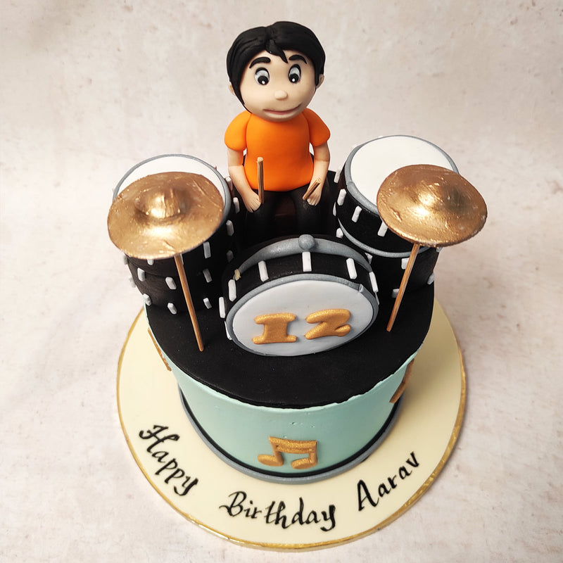 Placed on top of the birthday cake for kids is a figurine of a little boy passionately playing the drums, bringing the design to life and adding a touch of whimsy.